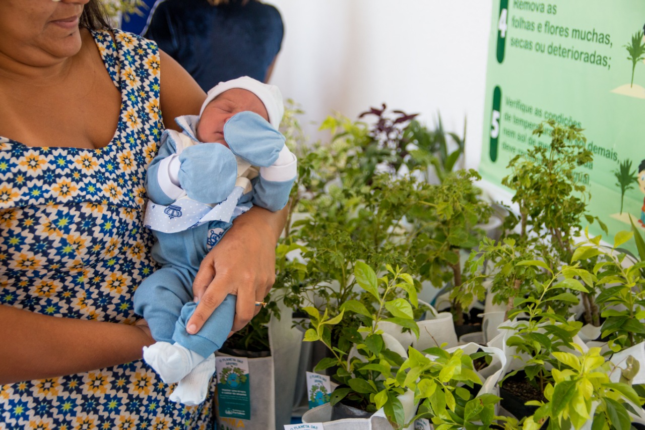 mulher segurando bebê recém-nascido ao lado de mudas de plantas